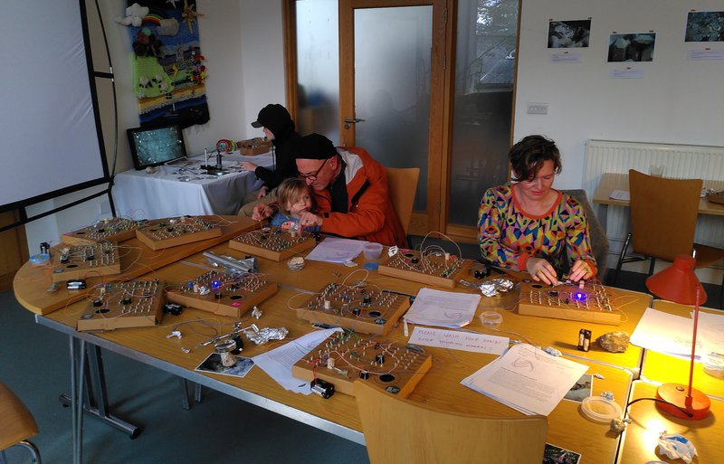 People building circuits, and one person looking at a smashed iPhone on a microscope in the background