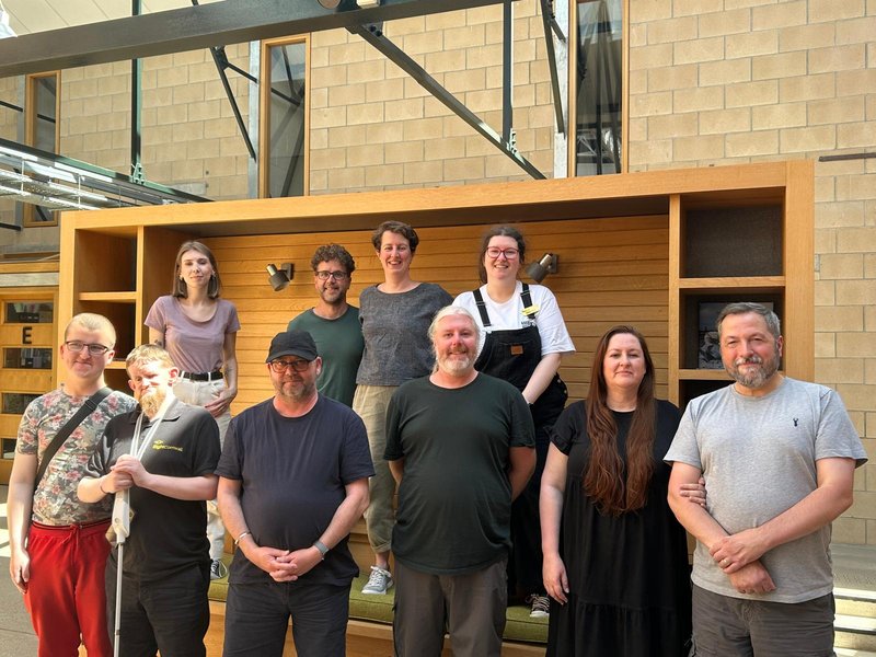 Photo of 10 people stood together, smiling and looking at the camera