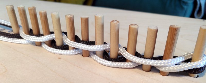 Wooden pegs with black and white threads woven between them
