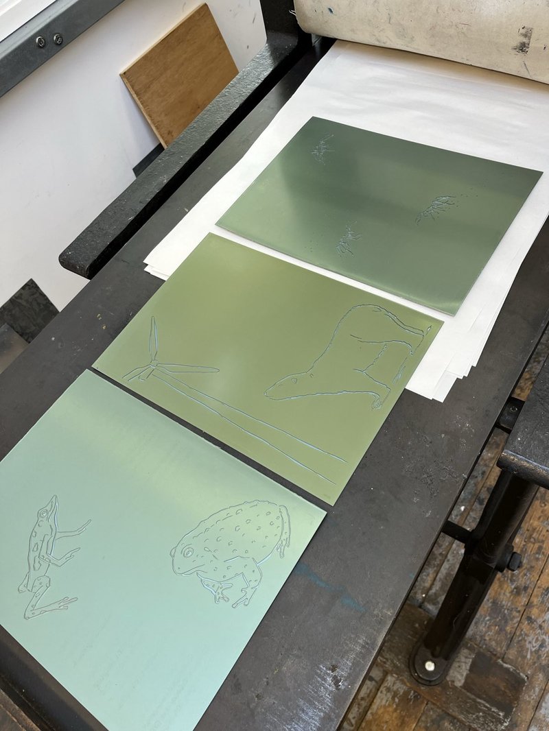 3 emboss plates on press, one is toads, another is a polar bear and turbine, and the final one is ants and their footsteps