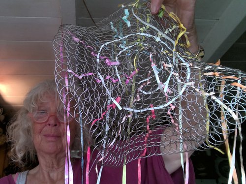 Photo of geraldine holding up a woven metal wire structure, with colourful ribbons threaded through it