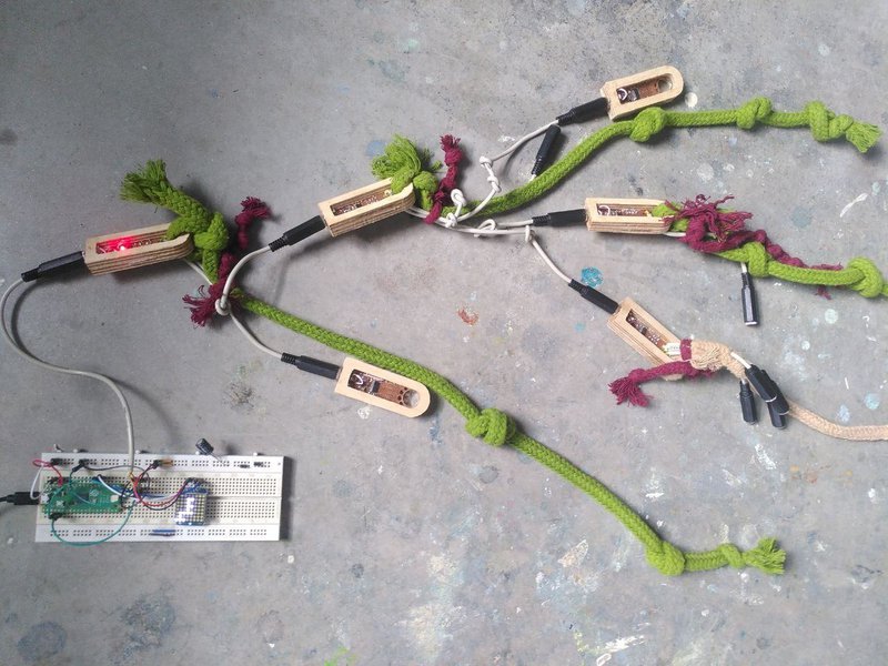 A network of small circuits inside wooden housings, some with coloured rope tied to them with patterns of knots indicating their ID. The tree structure is connected to a Raspberry Pi pico microcontroller with a small 8x8 LED screen that is showing a diagram representing the same hierarchical structure - which is able to be automatically read.