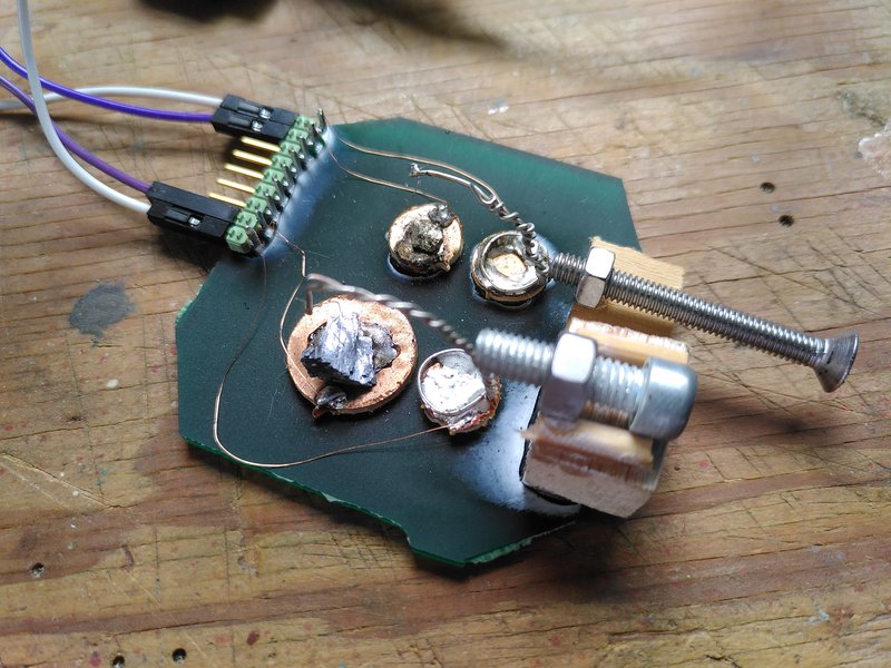 A brass coloured pyrite and silver galena crystals soldered to a small piece of copper clad board with two "cats whisker" wires "tickling" them. Nuts and bolts for fine tuning the pressure and connectors for attaching to a circuit.
