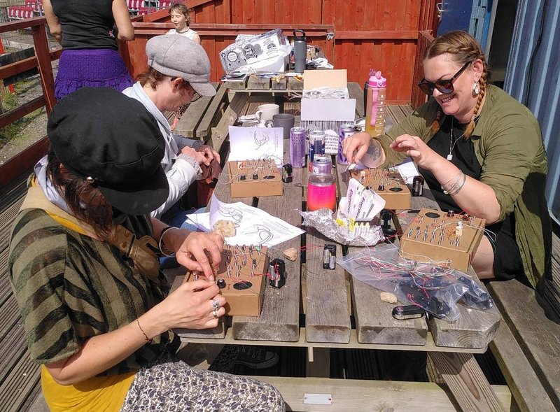 People sat on a picnic bench wiring together card board circuits in the sun.