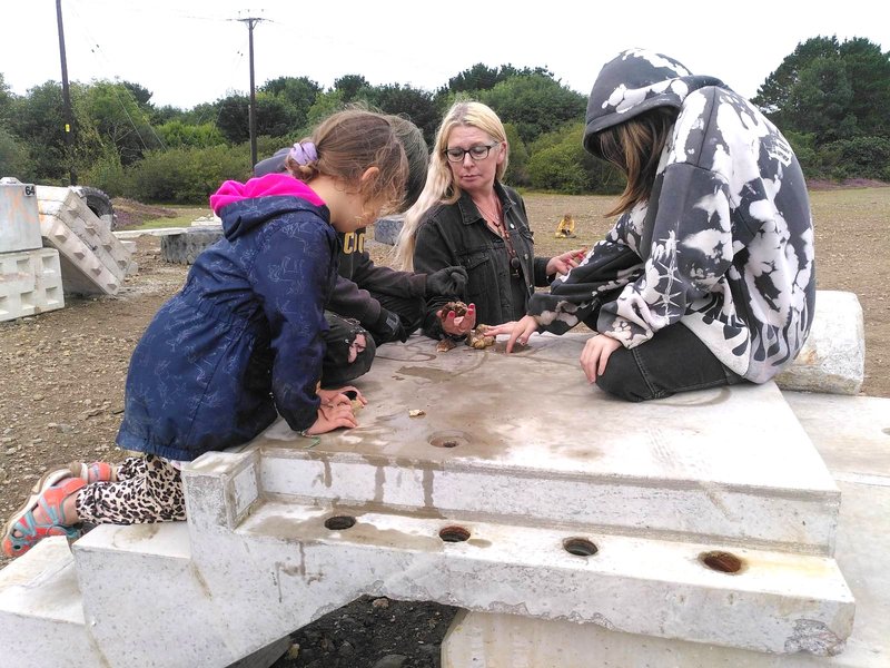 Four people sat on top of a concrete structure in abandoned mine examining rocks.