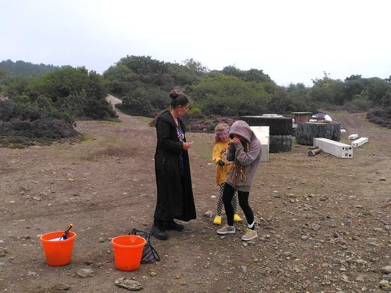 Three crystal hunters examining a find, with two bright orange buckets and gorse covered minewaste tailings mounds in the background